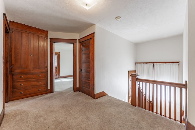 hallway with carpet, baseboards, a textured ceiling, and an upstairs landing