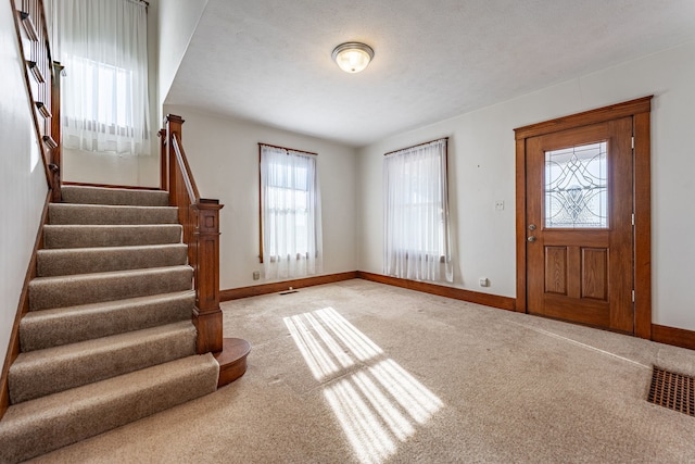 foyer featuring visible vents, stairs, baseboards, and light colored carpet