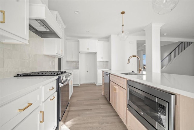 kitchen with decorative light fixtures, sink, white cabinets, stainless steel appliances, and light wood-type flooring