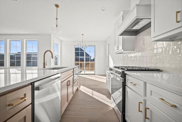 kitchen featuring sink, premium range hood, white cabinetry, appliances with stainless steel finishes, and decorative light fixtures