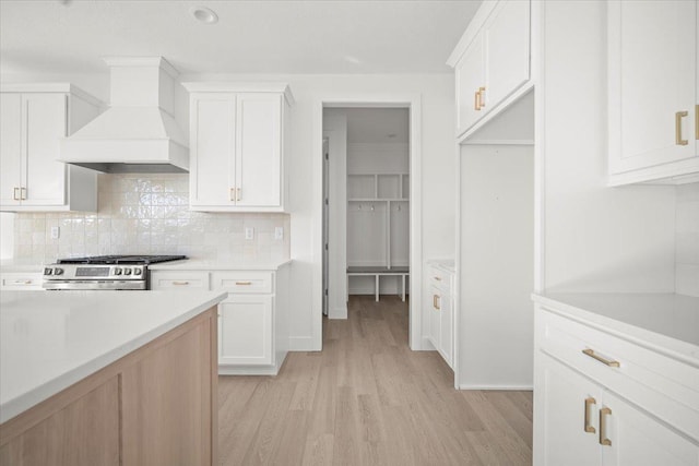 kitchen featuring stainless steel stove, white cabinetry, tasteful backsplash, light hardwood / wood-style floors, and custom exhaust hood