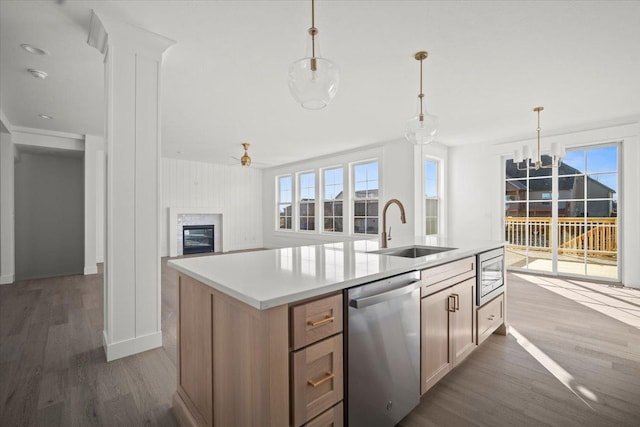 kitchen with pendant lighting, sink, stainless steel appliances, wood-type flooring, and a center island with sink