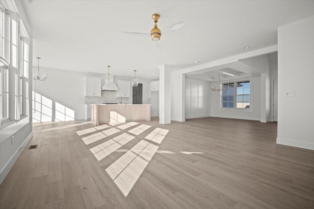 unfurnished living room with ceiling fan with notable chandelier and light hardwood / wood-style flooring