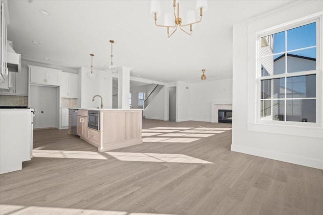 kitchen featuring pendant lighting, tasteful backsplash, an island with sink, white cabinets, and light hardwood / wood-style flooring