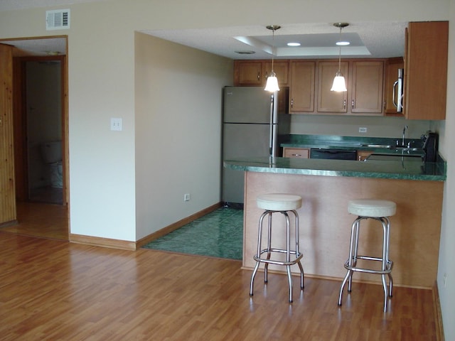 kitchen featuring light hardwood / wood-style flooring, hanging light fixtures, appliances with stainless steel finishes, a raised ceiling, and a breakfast bar