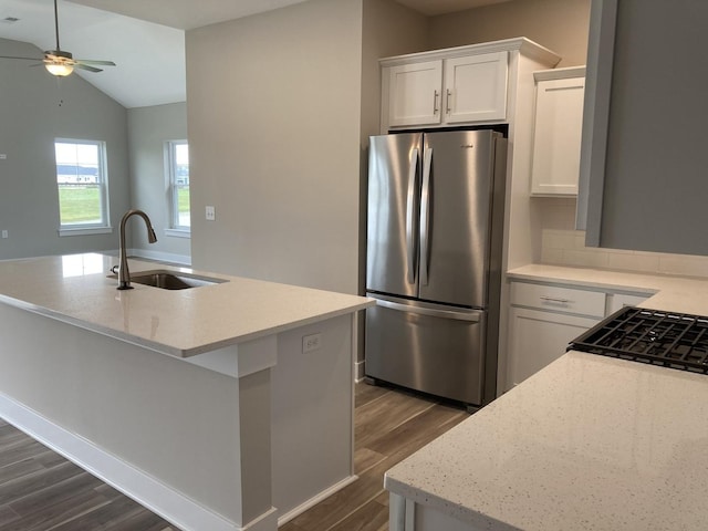 kitchen with light stone countertops, white cabinets, sink, stainless steel fridge, and a center island with sink