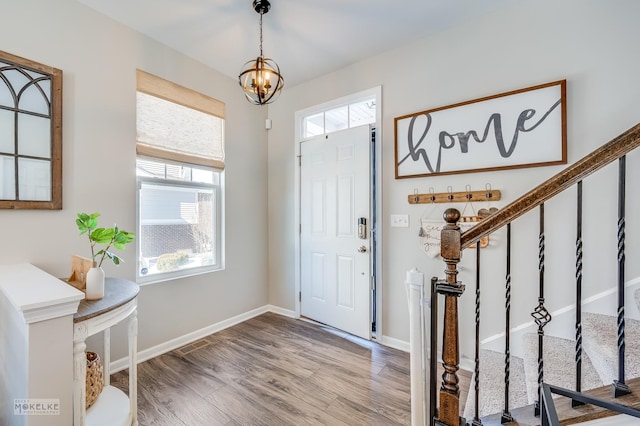 foyer entrance featuring baseboards, visible vents, stairway, a chandelier, and wood finished floors