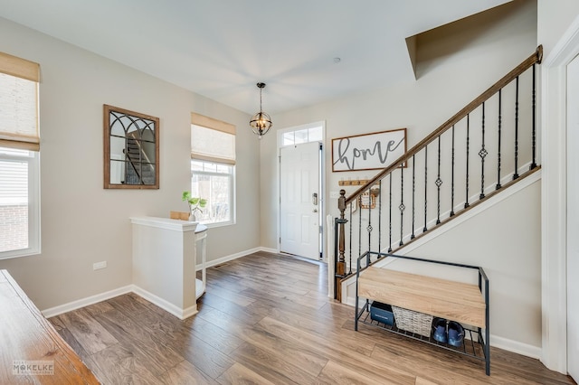 entryway featuring baseboards, a chandelier, stairway, and wood finished floors