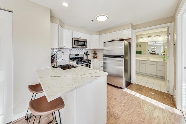 kitchen featuring white cabinets, a kitchen bar, stainless steel appliances, sink, and light stone counters