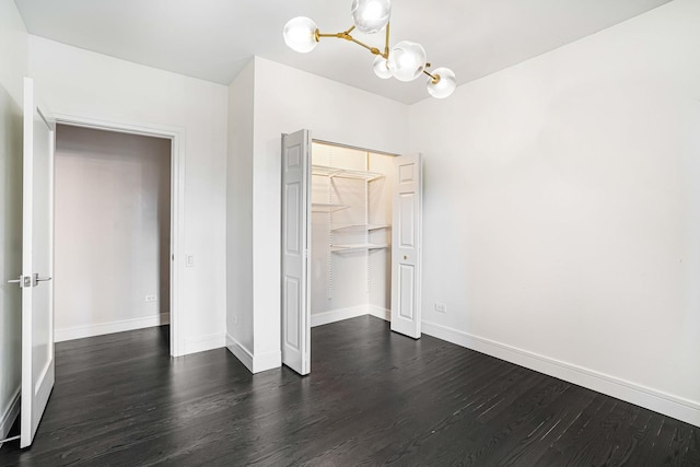 unfurnished bedroom with dark wood-type flooring, a chandelier, and a closet