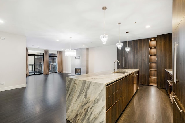 kitchen with a large island with sink, dark hardwood / wood-style flooring, sink, hanging light fixtures, and light stone counters