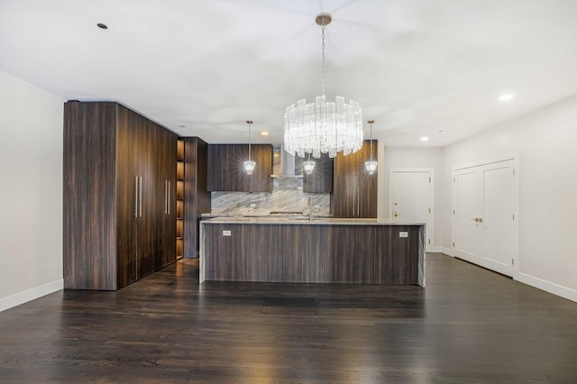 kitchen featuring decorative light fixtures, dark hardwood / wood-style flooring, tasteful backsplash, an island with sink, and dark brown cabinets