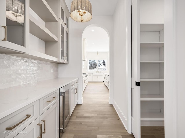 bar featuring pendant lighting, white cabinets, beverage cooler, light stone countertops, and light hardwood / wood-style flooring