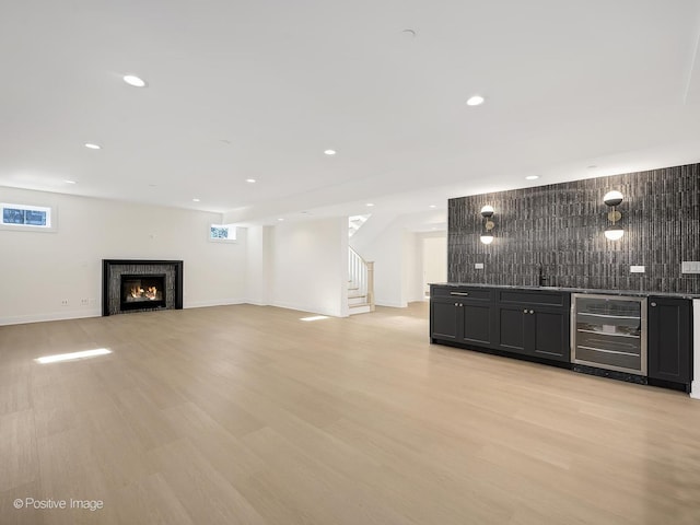 unfurnished living room featuring bar area, wine cooler, and light hardwood / wood-style flooring