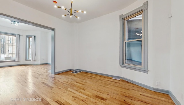 spare room with light hardwood / wood-style floors and an inviting chandelier