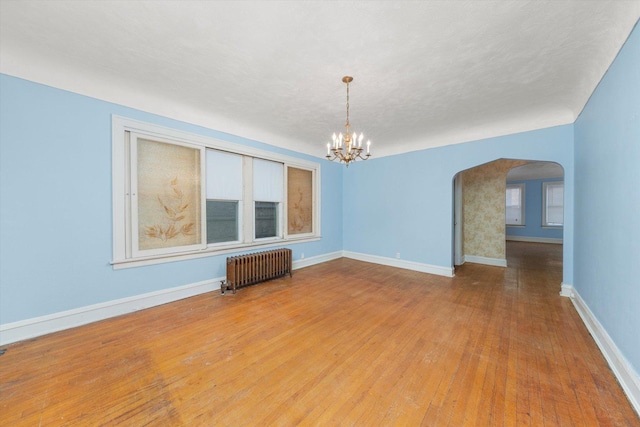 unfurnished living room featuring hardwood / wood-style floors, radiator, and a chandelier