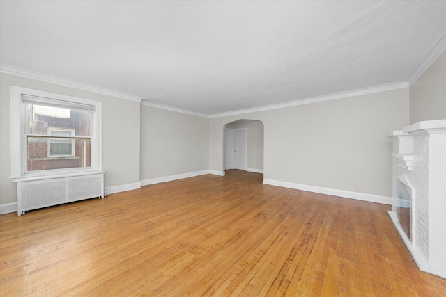 unfurnished living room with a brick fireplace, light hardwood / wood-style floors, radiator, and ornamental molding