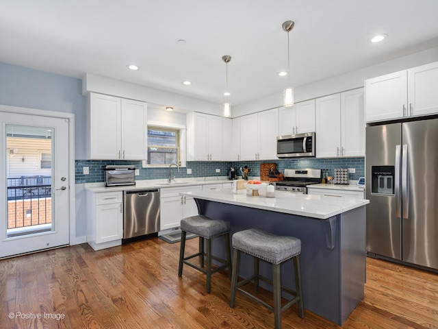 kitchen with dark wood-type flooring, hanging light fixtures, a kitchen island, stainless steel appliances, and white cabinets