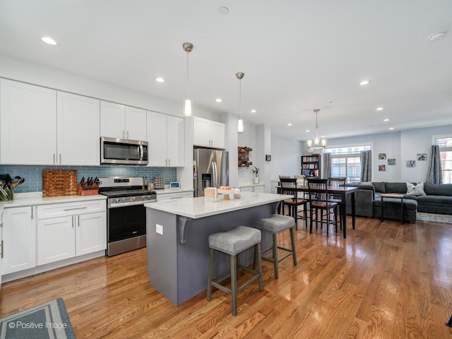 kitchen featuring stainless steel appliances, white cabinetry, hanging light fixtures, and a center island