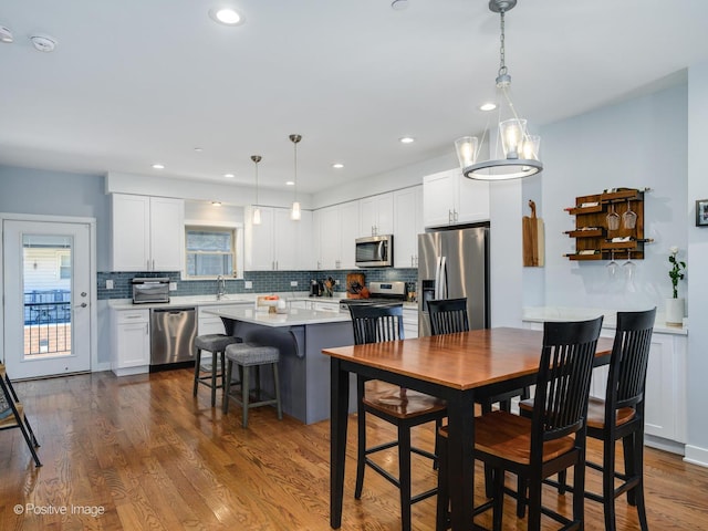 kitchen with a kitchen island, appliances with stainless steel finishes, dark hardwood / wood-style floors, decorative light fixtures, and white cabinetry