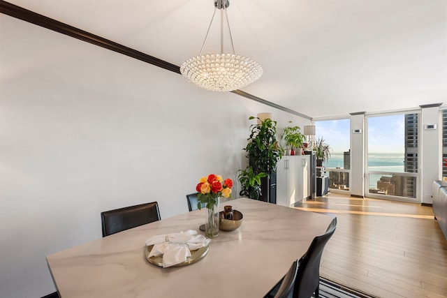 dining space featuring wood-type flooring, a wall of windows, ornamental molding, a water view, and an inviting chandelier