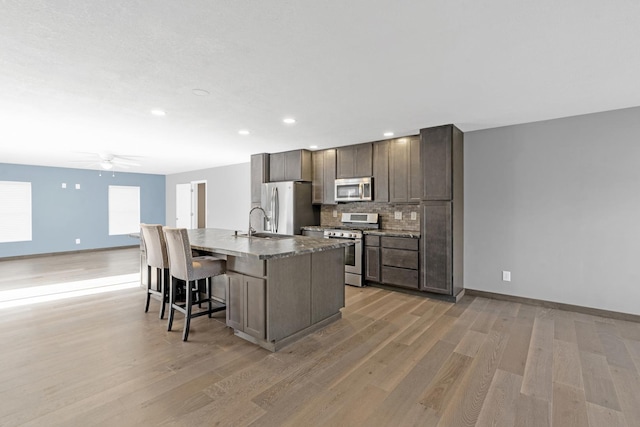 kitchen featuring a breakfast bar, sink, an island with sink, stainless steel appliances, and backsplash