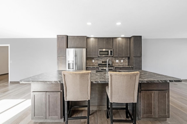 kitchen featuring dark brown cabinetry, stainless steel appliances, an island with sink, and a breakfast bar area