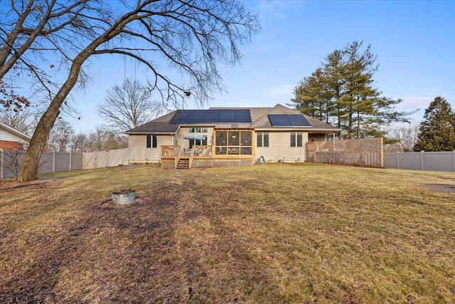 rear view of house with a wooden deck, a yard, and solar panels