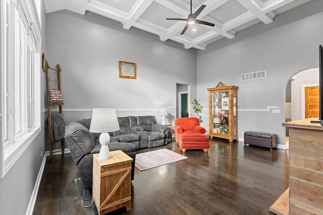 living room with a towering ceiling, coffered ceiling, ceiling fan, dark wood-type flooring, and beam ceiling