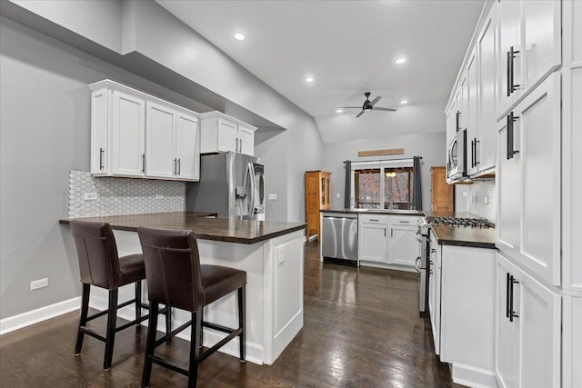 kitchen with a breakfast bar, appliances with stainless steel finishes, kitchen peninsula, ceiling fan, and white cabinets