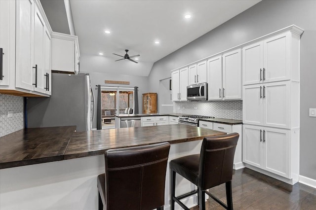 kitchen featuring a breakfast bar area, white cabinetry, wooden counters, kitchen peninsula, and stainless steel appliances