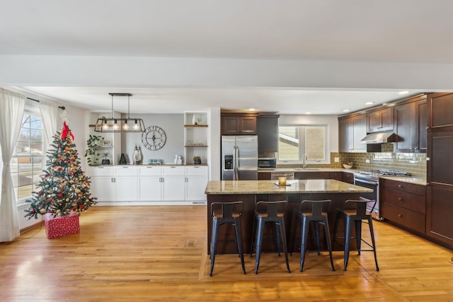 kitchen with sink, appliances with stainless steel finishes, hanging light fixtures, dark brown cabinetry, and a kitchen island