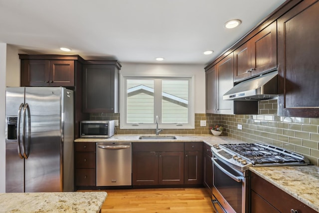 kitchen with dark brown cabinetry, sink, light hardwood / wood-style flooring, stainless steel appliances, and light stone countertops