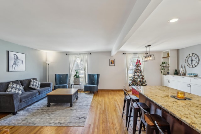 living room with beam ceiling, light hardwood / wood-style floors, and bar area