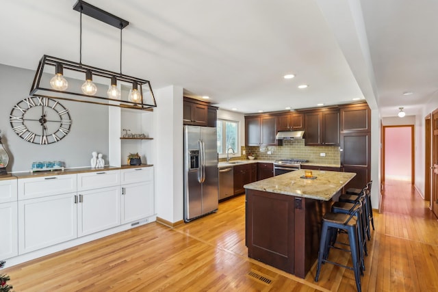 kitchen featuring stainless steel appliances, sink, light wood-type flooring, and decorative light fixtures