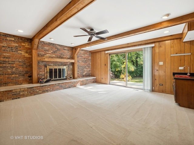 unfurnished living room with light carpet, ceiling fan, sink, wood walls, and a brick fireplace