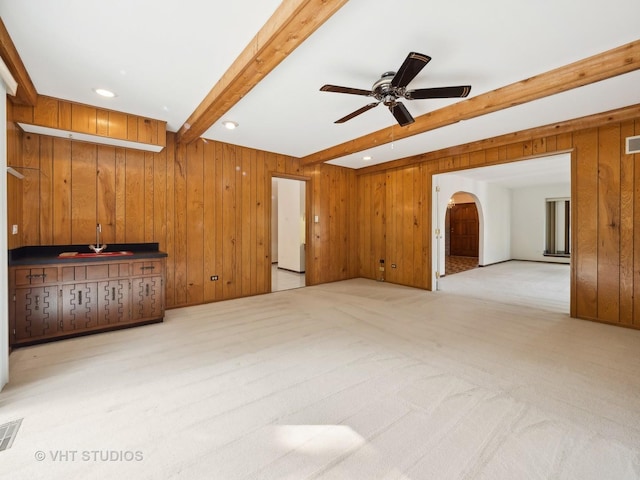 carpeted living room featuring wooden walls, beam ceiling, and ceiling fan