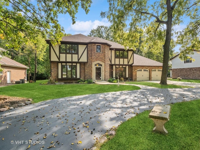 tudor-style house featuring a garage, central AC unit, and a front yard