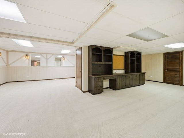 basement featuring built in desk, carpet flooring, and a paneled ceiling