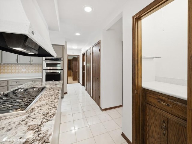 kitchen featuring decorative backsplash, light stone countertops, appliances with stainless steel finishes, and light tile patterned flooring