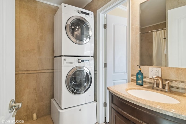 clothes washing area featuring tile walls, sink, crown molding, and stacked washer and dryer