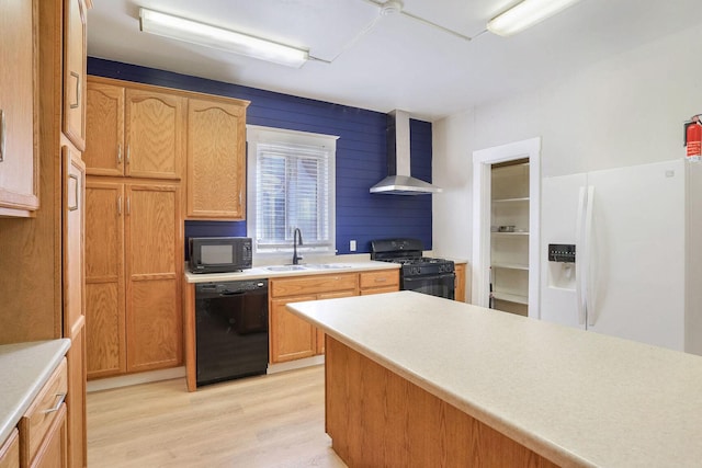 kitchen with sink, wall chimney range hood, light hardwood / wood-style flooring, wooden walls, and black appliances