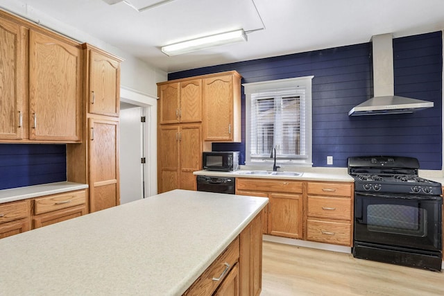 kitchen featuring sink, black appliances, light hardwood / wood-style floors, wall chimney exhaust hood, and wood walls