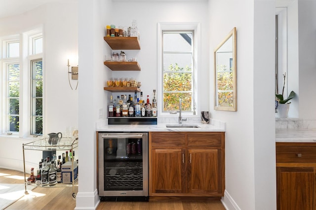 bar featuring beverage cooler, sink, and light wood-type flooring