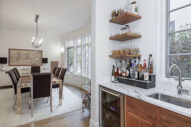 bar featuring pendant lighting, sink, wine cooler, light stone countertops, and light wood-type flooring