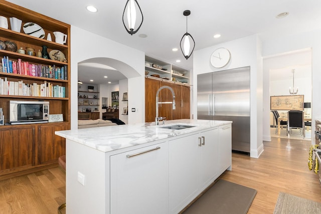 kitchen featuring pendant lighting, an island with sink, sink, white cabinets, and light stone counters