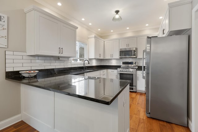 kitchen with white cabinetry, wood-type flooring, dark stone countertops, kitchen peninsula, and stainless steel appliances