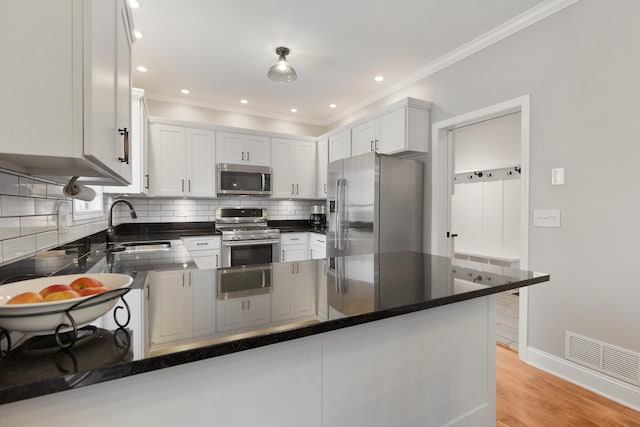 kitchen featuring sink, appliances with stainless steel finishes, white cabinetry, decorative backsplash, and kitchen peninsula