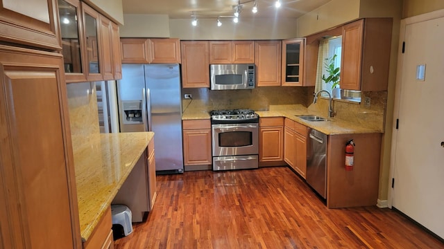 kitchen with dark wood-type flooring, sink, stainless steel appliances, light stone countertops, and backsplash