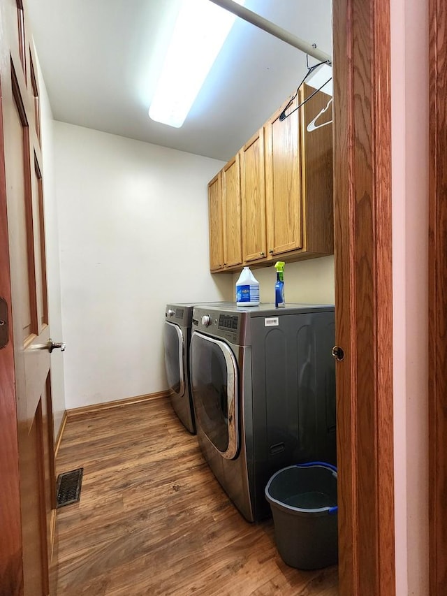 laundry room featuring hardwood / wood-style flooring, washing machine and clothes dryer, and cabinets